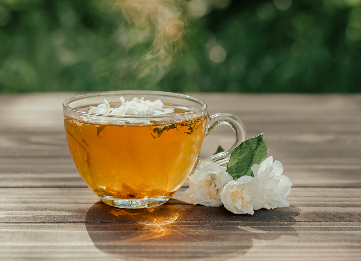 Steaming cup of tea with flowers on a wooden surface